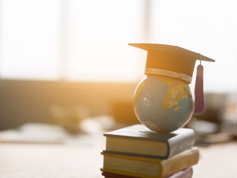 Academische hoed op stapel boeken en wereldbol